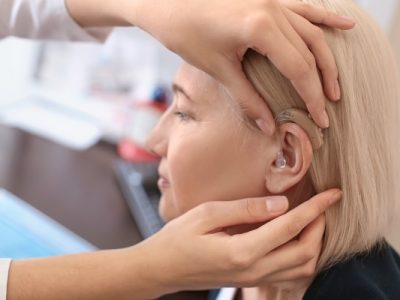 Otolaryngologist putting hearing aid in woman's ear in hospital