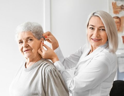 Otolaryngologist putting hearing aid in senior woman's ear in hospital