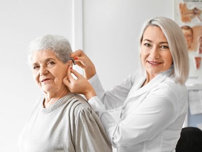 Otolaryngologist putting hearing aid in senior woman's ear in hospital